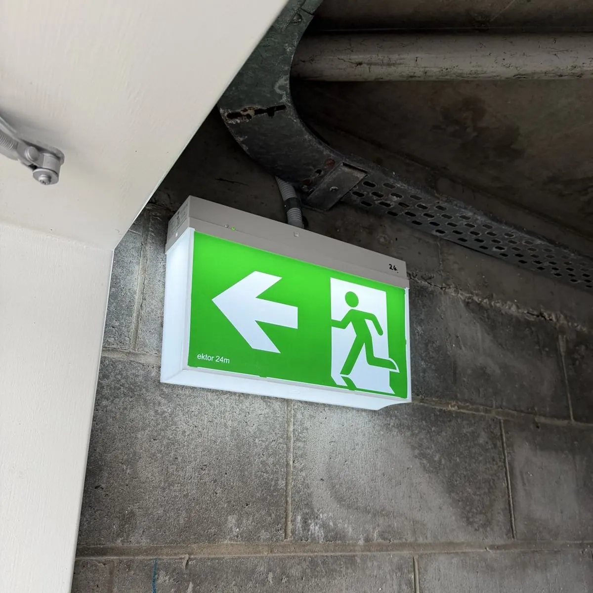 An illuminated green emergency exit sign mounted on a block wall