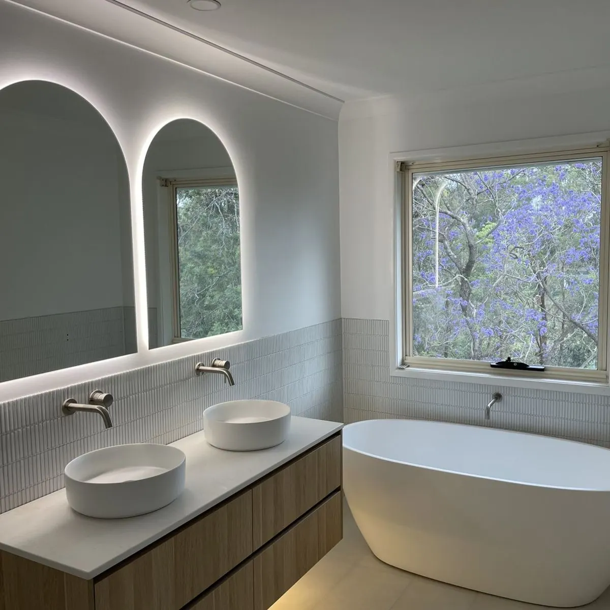 Backlit arch mirrors and under-vanity lighting in a renovated bathroom